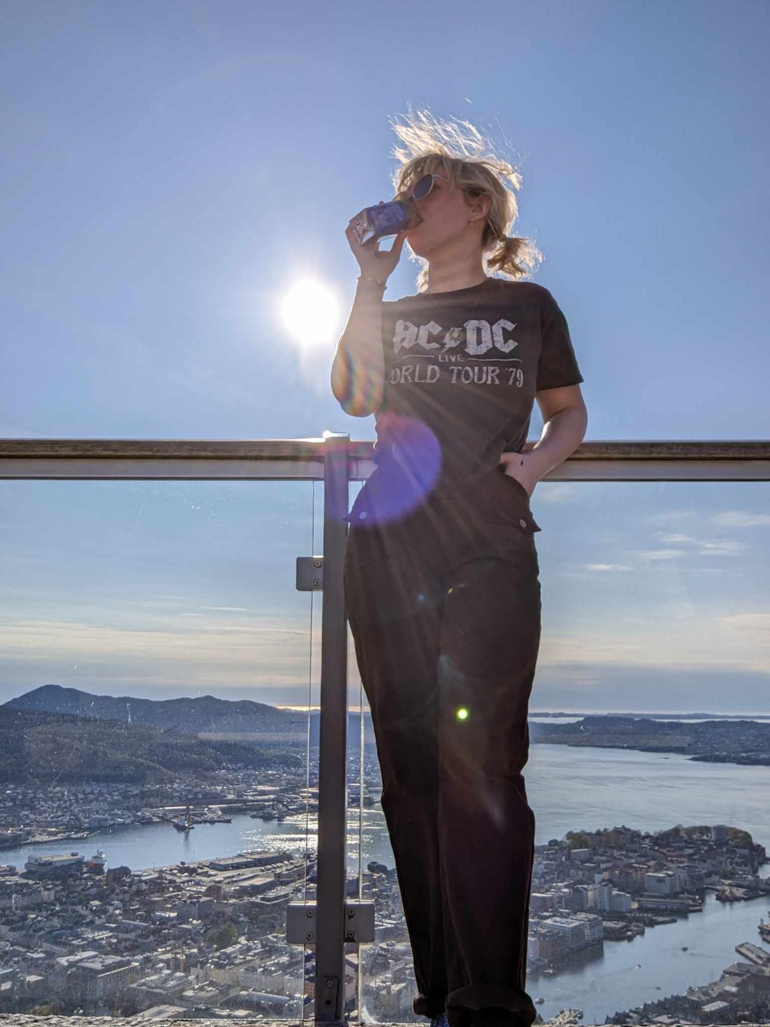 A picture of a young woman standing against a glass fence, with the view of Bergen city.